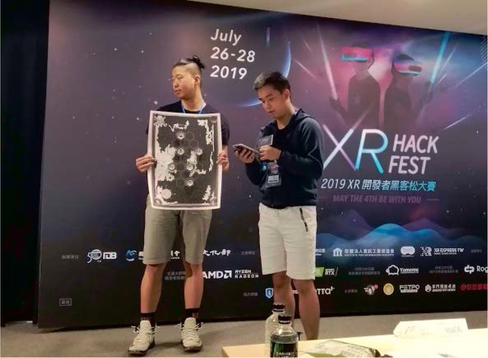 黃聖為同學(右)、羅郁翔同學(左)代表「馬頭姑娘」上台簡報，展示自行設計的AR掃描物